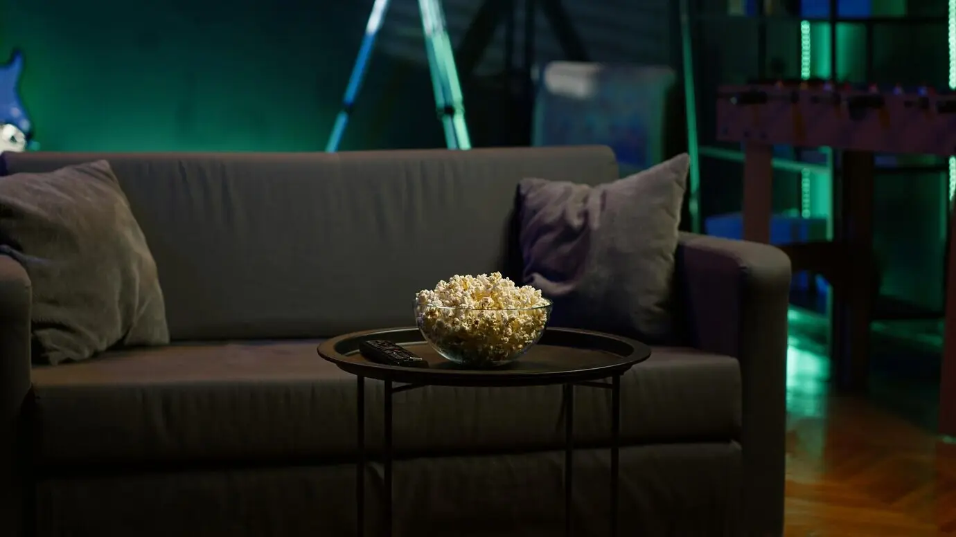 A bowl of popcorn on a table in an empty, neon-lit, cozy residential interior.