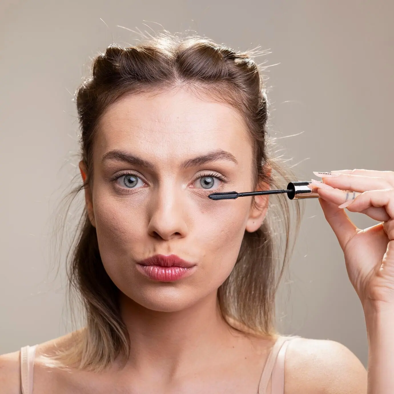 A radiant female model wearing minimal makeup applies mascara for thick lashes and has a glowing complexion.